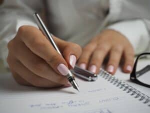 woman in white long sleeved shirt holding a pen and writing on paper
