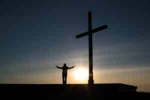 silloette of person standing beside cross during sunset